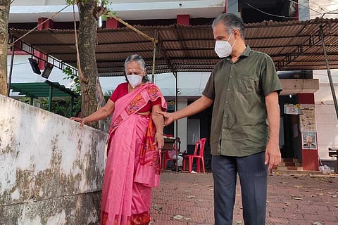 An elderly woman being assisted by a man as she comes out of a polling booth in Kerala