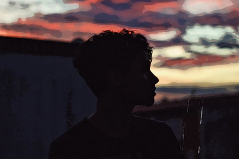 Silhouette of a person against dark skies, as they look beyond the horizon to the right of the frame.