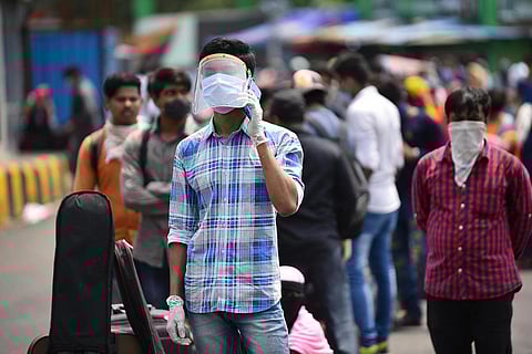 Migrants and Stranded passengers wait outside Secunderabad Railway Station to board trains as Indian Railways resume transport services, a man wearing a mask and a white and blue checks shirt is seen talking on the mobile.