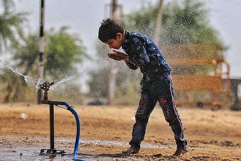 A boy cools down himself by standing against sprinkling water