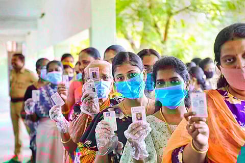 Women standing in line wearing masks and holding up voter ID