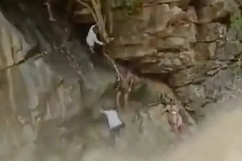 A rock above gushing water and rescue officials saving a mother and child using a rope