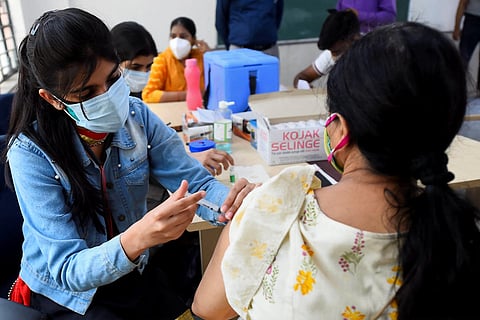 A young woman wearing a blue shirt is seen vaccinating a woman wearing a creme salwar