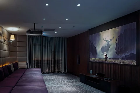 Image of sofa at one end of a room with a movie being projected on the wall opposite