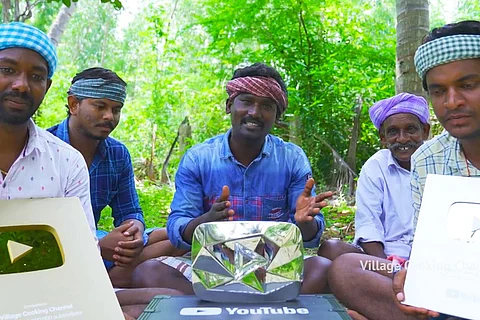Team of Village Cooking channel displaying diamond button from YouTube while sitting on the ground