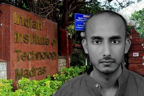A black and white image of IIT Madras Assistant prof Vipin Veetil who is wearing a collared t-shirt, the IIT Madras board in the background