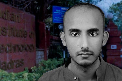 A black and white image of IIT Madras Assistant prof Vipin Veetil who is wearing a collared t-shirt, the IIT Madras board in the background