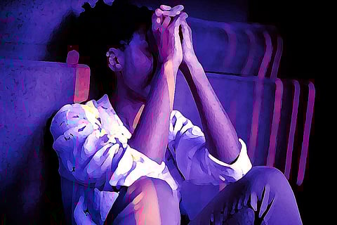 A woman sitting against a wall, upset