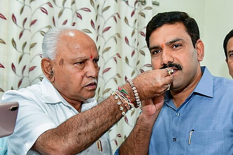 BS Yediyurappa hand feeding a sweet to his son BS Vijayendra