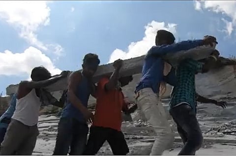 A group of male labourers carrying a stone column on their shoulders