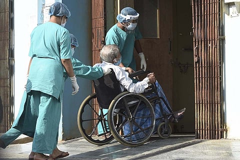 Healthcare Workers in green uniform moving a patient in a wheel chair inside a hospital