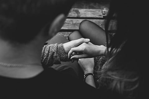 A black and white photo of a couple holding hands while sitting on a bench