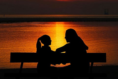 Silhouette of adult and child talking in front of a water body