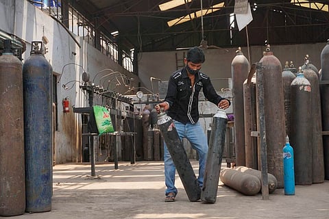 A worker in jeans, black shirt and mask handling oxygen cylinders at a refilling plant