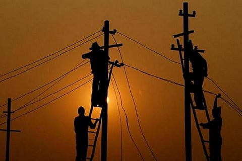 Silhouette of people working on an electric pole