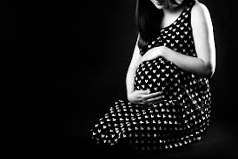 Pregnant woman wearing a black dress and holding her abdomen.