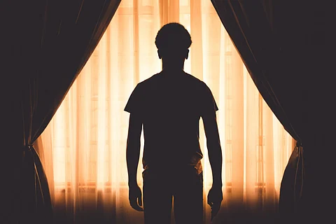 Silhouette of a man standing in front of a softly lit curtain, framed by dark drapes on both sides.
