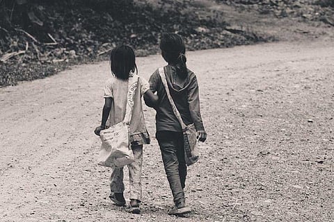 Two minor girls holding hands and walking in a field