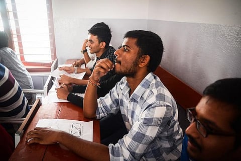 Three male students sitting at a wooden bench with pieces of paper in front of them