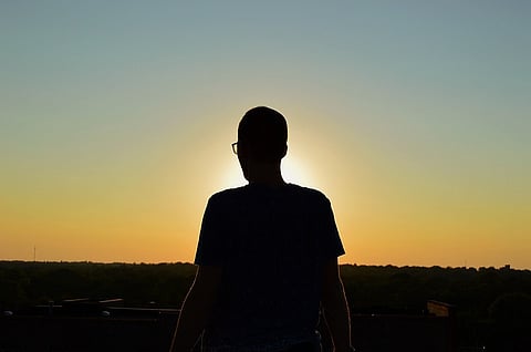 Silhouette of a man wearing spectacles, standing against the sun.