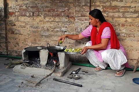 A woman in a pink kurta and red dupatta squatting beside a wood fire stove and cooking
