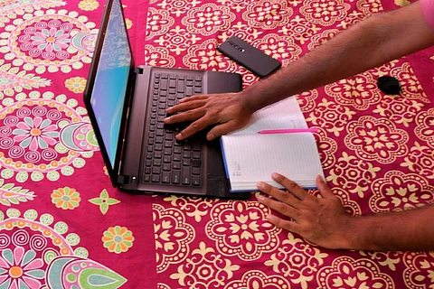 A person working on their laptop from home while taking notes