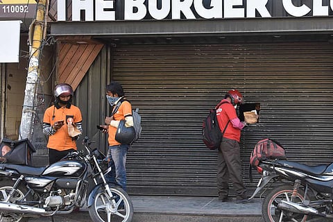 Two Swiggy delivery executives talk to each other while a Zomato delivery rider collects a food parcel 