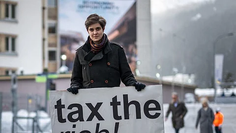 Austrian Marlene Engelhorn, who inherited from her family who owns the Germany’s chemical giant BASF, poses with a placard reading “Tax the rich!” at the entrance of the Congress center on the opening of the annual meeting of the World Economic Forum (WEF) in Davos, on 15 January 2024. (Photo by Fabrice COFFRINI / AFP)