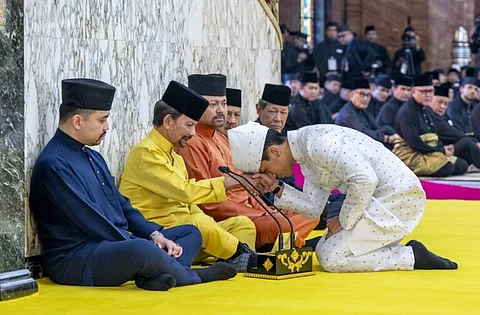 This handout picture taken by Brunei’s Information Department on 11 January 2024 and released on 12 January 2024 shows Brunei’s Prince Abdul Mateen (R) touching his forehead on his father’s hand, Brunei’s Sultan Haji Hassanal Bolkiah (2nd L), after his solemnization at Sultan Omar Ali Saifuddien Mosque in Bandar Seri Begawan. (Photo by Handout / Brunei’s Information Department / AFP)