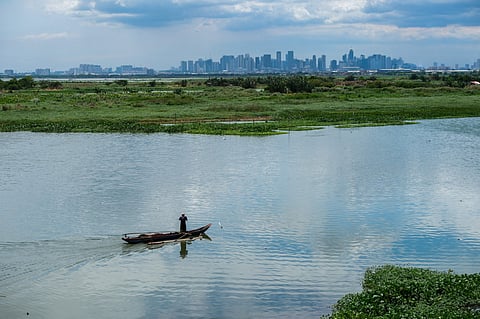 A fisherman floats past the cityscape view of Metro Manila while waiting for his catch. Laguna de Bay, Angono, Rizal. 4 June 2023.