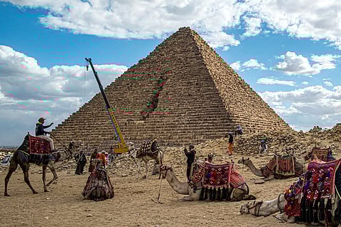 A crane lifting stones is pictured behind camels resting with their trainers by the Pyramid of Menkaure (or Menkheres, built in the 26th century BC) at the Giza Pyramids Necropolis, west of Cairo, on 29 January 2024. In a video posted on Facebook on 26 January, Mostafa Waziri, the head of Egypt's Supreme Council of Antiquities, showed workers setting blocks of granite on the base of the pyramid, dubbing it "the project of the century." When originally built, the pyramid was encased in granite, but over time lost part of its covering. The renovation aims to restore the structure's original style by reconstructing the granite layer.