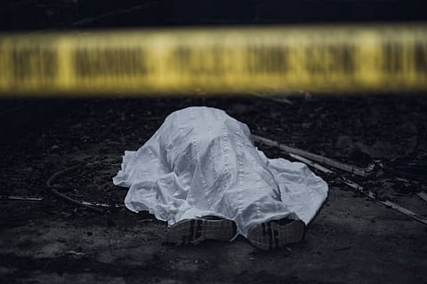 Dead body under a white sheet of cloth behind a police line
