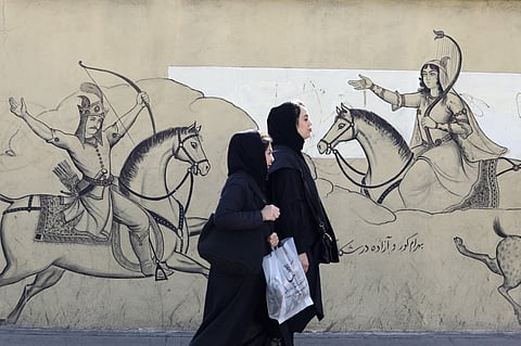 Fully-veiled women walk past a mural illustration depicting scenes from the epic Persian poem "Shahnama" (Book of Kings) in central Tehran on January 30, 2024.