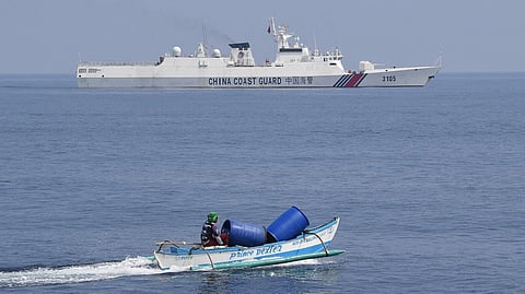 (FILES) This photo taken on 20 September 2023 shows a Philippine fisherman aboard his outrigger boat sailing past a Chinese coast guard ship near the Chinese-controlled Scarborough Shoal in waters of the disputed South China Sea. China, which claims sovereignty over almost the entire South China Sea, snatched control of Scarborough Shoal from the Philippines in 2012. Since then, it has deployed coast guard and other vessels to block or restrict access to the fishing ground that has been tapped by generations of Filipinos. (Photo by Ted ALJIBE / AFP)