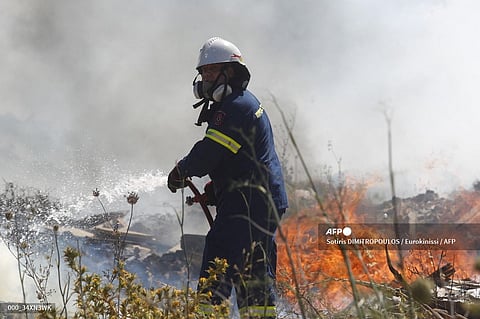 A firefighter uses a hose as he attempts to extinguish flames after a wildfire broke out in Kitsi, a southern suburb of Athens on June 19, 2024. An early heatwave has already gripped Greece, prompting authorities there to close the Athens Acropolis and other tourist attractions during the hottest hours of the day.