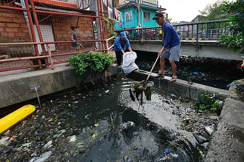 DEPARTMENT of Environment and Natural Resources workers scoop up waste from a creek during a cleanup duty.