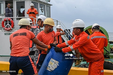 Coast guard personnel and crew of a private company load a barrel of oil spill dispersant to be used in the oil spill response, at a port in Limay, Bataan on July 26, 2024. A Philippine-flagged tanker carrying 1.4 million litres of industrial fuel oil capsized and sank off Manila on July 25, authorities said, as they raced against time to contain the spill.