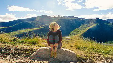 A woman sits peacefully in nature, her eyes closed as she listens intently to the symphony of sounds around her – a perfect embodiment of World Listening Day's spirit.