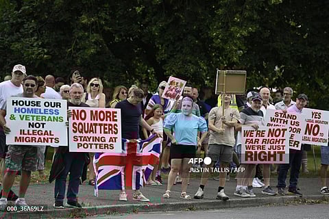 Protesters, including one wearing a mask of Britain's Prime Minister Keir Starmer, hold placards during a 'Enough is Enough' demonstration called by far-right activists near a hotel housing asylum seekers in Aldershot on August 4, 2024. Far-right protesters clashed with British police during tense rallies as unrest linked to disinformation about a mass stabbing that killed three young girls spread across the UK.