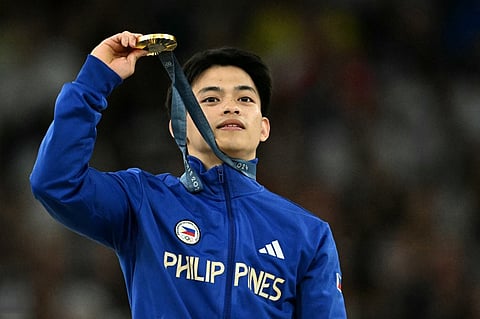 Carlos Yulo proudly shows off the gold medal after winning the floor exercise in the Paris Olympics.