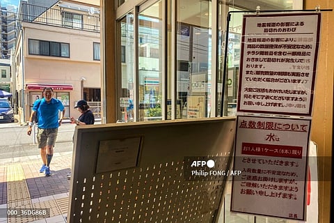 Customers walk by the entrance of a supermarket as signs written "quake-related media reports are causing some products to run out of stocks and that sales restrictions are likely" (up) and "bottled water is being rationed, with a cap of one case (six bottles) per each customer" in Sumida district of Tokyo on August 10, 2024. Authorities in Japan are urging the public to avoid hoarding as anxiety over a possible megaquake has triggered a spike in demand for disaster kits and daily necessities.