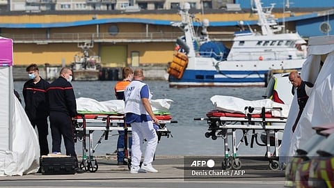 Firefighters and Civil Protection agents stand next to body bags of migrants on pier next to the water