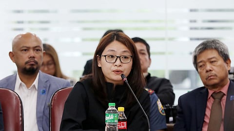 Dismissed Bamban town Mayor Alice Guo speaks into a microphone during the Quad Committee hearing at the House of Representatives on Thursday. The inquiry focuses on the connection between Philippine Offshore Gaming Operators (POGOs) and the country’s illegal drug trade. A nameplate reading "Alice Leal Guo" and two bottled drinks are visible in front of her.