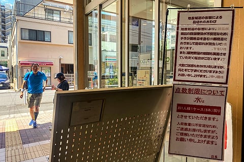 Customers walk by the entrance of a supermarket as signs written "quake-related media reports are causing some products to run out of stocks and that sales restrictions are likely" (up) and "bottled water is being rationed, with a cap of one case (six bottles) per each customer" in Sumida district of Tokyo on August 10, 2024. Authorities in Japan are urging the public to avoid hoarding as anxiety over a possible megaquake has triggered a spike in demand for disaster kits and daily necessities.
