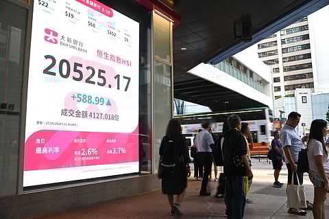 Pedestrians walk past a sign showing the numbers of the Hang Seng Index in Hong Kong. Hong Kong stocks soared more than three percent on 27 September, capping its best week since the global financial crisis, fueled by a series of Chinese measures this week aimed at kickstarting the economy.