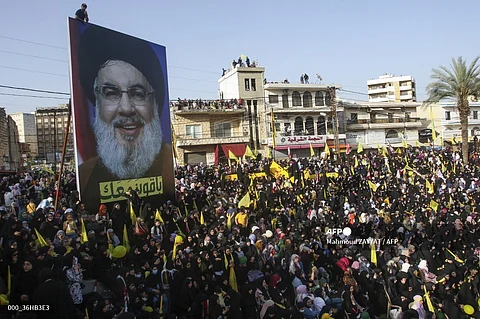Supporters of Lebanon's Iran-backed Shiite group Hezbollah, wave the group's, Lebanese, and Iranian flags as they rally to attend a speech by Hezbollah leader Hassan Nasrallah (billboard portrait), broadcast on a giant screen, in the southern city of Nabatiyeh, on 9 May, 2022. Israel's military announced on September 28, 2024 that Nasrallah was killed in an Israeli strike on Beirut the previous night, but there was no confirmation from the Lebanese armed group.