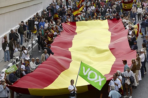 A woman waves a flag of far-right VOX political party as others carry a giant Spanish flag during a demonstration to protest against the ruling government and to demand general elections, in Madrid on 20 October, 2024. Thousands of people packed a Madrid square today to protest against Socialist Prime Minister Pedro Sanchez's government and demand an early election, at a rally backed by right-wing parties. Waving Spanish flags, protesters massed in the Plaza de Castilla square in the heart of Madrid's financial district and called on Sanchez to resign, shouting "traitor". More than 100 little-known, small groups linked to the right and far-right called the rally under the slogan "For unity, dignity, the law and freedom. General elections now!".