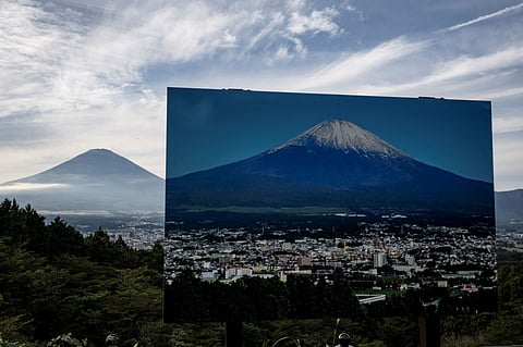 A sign with a photo of Mount Fuji covered in snow is seen at a view point as Mount Fuji, the highest mountain in Japan at 3,776 metres, looms in the background in Gotemba, Shizuoka prefecture on 31 October, 2024. Japan's Mount Fuji remained snow-less on 31 October — the latest date that its majestic slopes have been bare since records began 130 years ago.