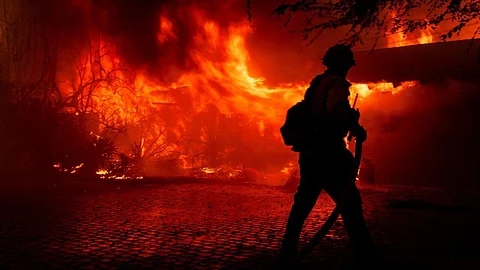 A firefighter tries to control the fire burning down a house as the Mountain Fire scorches acres, the wildfire fueled by strong Santa Ana winds, in Camarillo, California, on 6 November, 2024.
