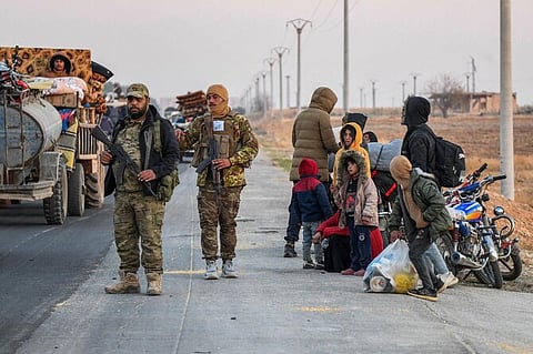 Anti-regime fighters stand on the roadside as displaced Syrian Kurds drive vehicles loaded with belongings on the Aleppo-Raqqa highway to flee areas on the outskirts of the northern city of Aleppo which were formerly controlled by the Kurdish-led Syrian Democratic Forces (SDF), after they were seized by Islamist-led rebels on December 2, 2024.